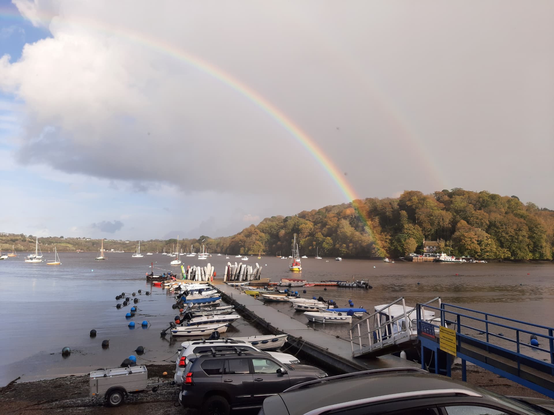 Boats moored at a tidal marina pontoon under a rainbow after rain