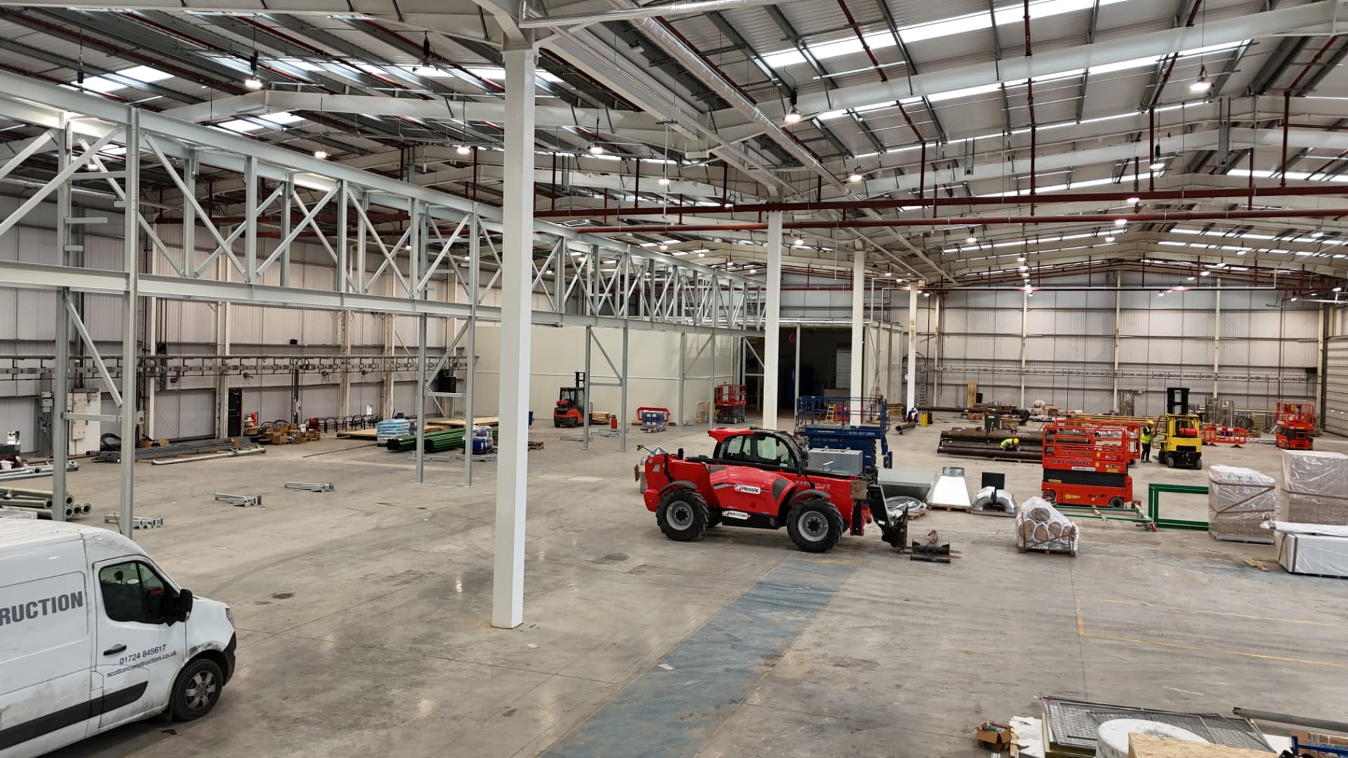 Interior of a new manufacturing facility being fitted out, with a telehandler, scissor lifts, forklifts and building materials on the concrete floor