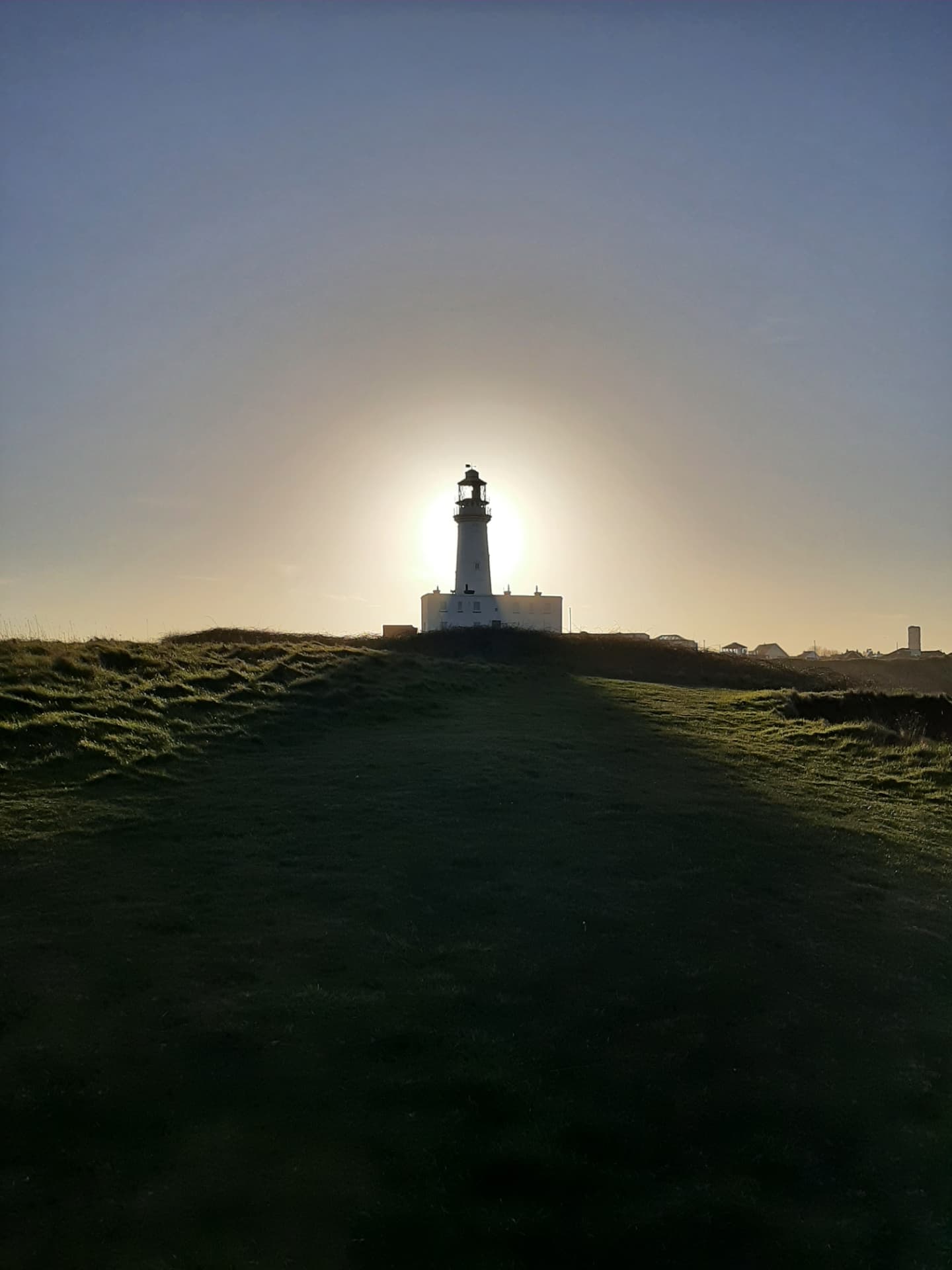 Coastal lighthouse in low sunlight above open grassland
